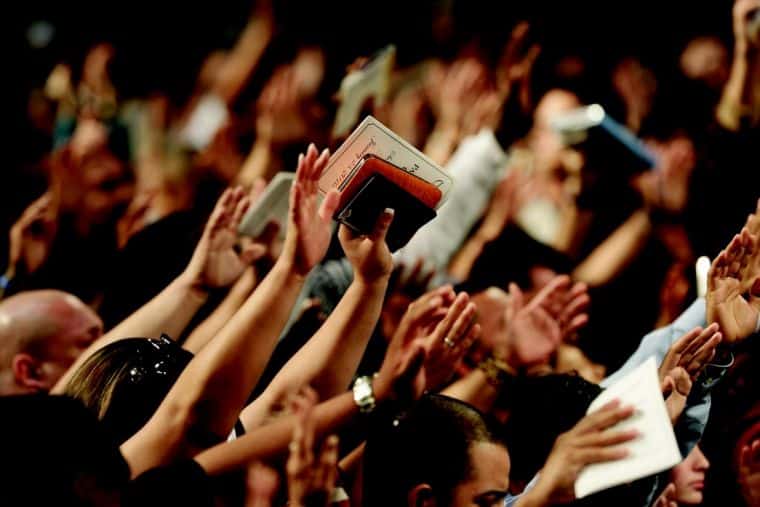 People raising their hands in worship, holding religious texts at a faith gathering, s